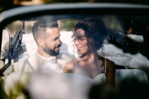 Sposi seduti in auto d’epoca si guardano con complicità dopo il matrimonio, fotografia di matrimonio naturale ed emozionale, editorial.